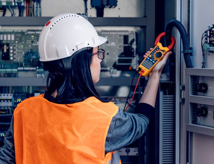 Electrical technician using a multimeter to check the voltage on a control panel.
