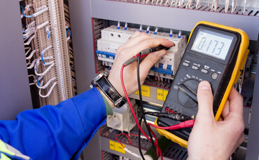 Electrician using a multimeter to test a control panel.