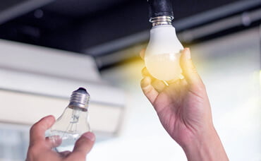 Changing a light bulb: hand replacing an old bulb with a new, illuminated one.